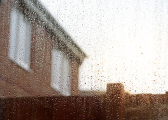 Rain drops on glass door with blurry house and wooden fence in background, Rainy season, Droplet surface on glass window,View through the window to garden inside house