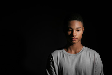 Sad African-American teenage boy on dark background