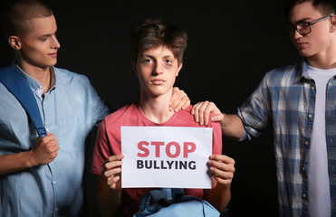 Boy with sheet of paper and aggressive teenagers on dark background