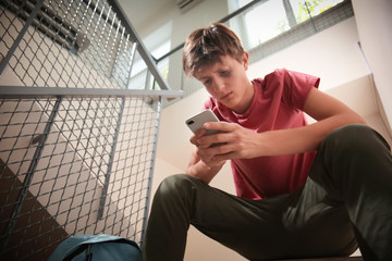 Sad teenage boy with mobile phone sitting on stairs. Bullying at school