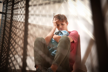 Sad teenage boy sitting on stairs. Bullying at school