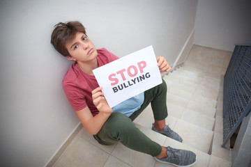 Teenage boy holding sheet of paper with text STOP BULLYING at school