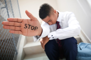 African-American teenage boy with word STOP written on hand sitting on stairs at school