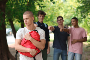 Bullied teenage boy with aggressive schoolmates outdoors