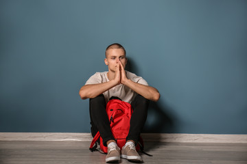 Sad teenage boy sitting near color wall indoors. Bullying at school