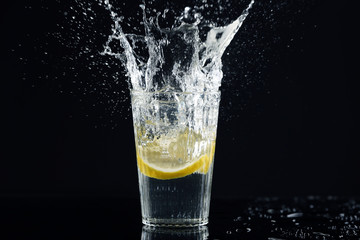 Glass of fresh lemonade with splashes on dark background