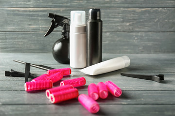Hair curlers with cosmetics on wooden table
