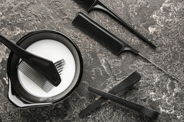 Bowl with hair dye, combs and clips on grey background
