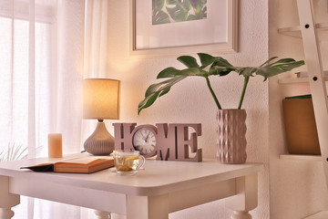 Tropical leaves in vase with decorative clock and open book on table in room