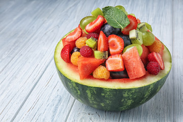 Delicious fruit salad in watermelon bowl on light wooden table