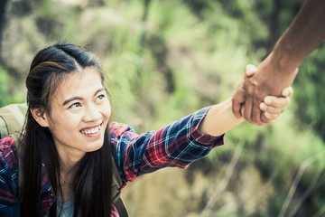 Young tourists with backpacks, athletic boy helps slim girl to clime rocky mountain top against...