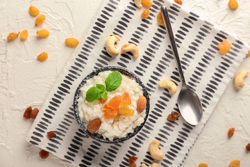 Delicious rice pudding with dried fruits and almonds in bowl on light table