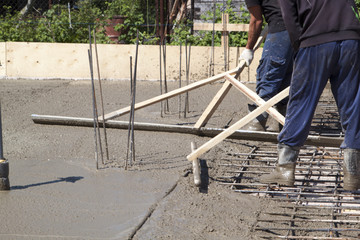 two workers leveling fresh concrete slab with a special working tools