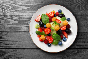 Plate with delicious fruit salad on dark wooden table