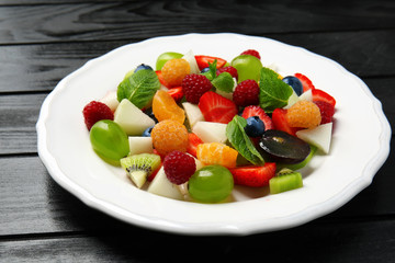 Plate with delicious fruit salad on dark wooden table
