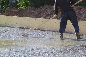 worker leveling fresh concrete slab with a special wooden working tool