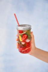 Woman holding jar of fresh strawberry lemonade on light background