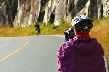 Biker photographer in raincoat and helmet takes picture of a cyclist on the road