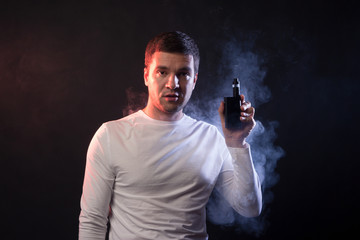 Man is smoking vape. Portrait in studio on a black background. Concept of tobacco dependence