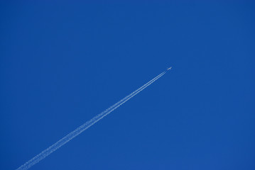 Jet streaking across blue sky with contrails