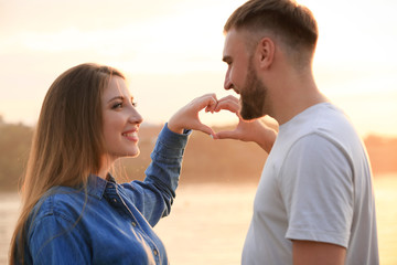 Happy couple making heart with their hands near river