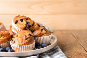 Plate with tasty blueberry muffins on wooden table