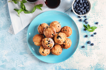 Plate with tasty blueberry muffins on color table