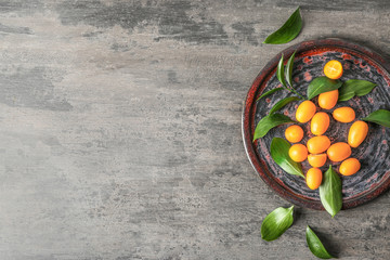Plate with delicious kumquat fruit on grey table