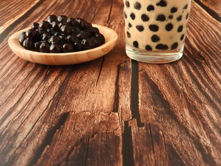 Fototapeta na wymiar A glass cup of pearl milk tea (also called bubble tea) and a plate of tapioca ball on wooden background. Pearl milk tea is the most representative drink in Taiwan. Taiwan food . With copy space.