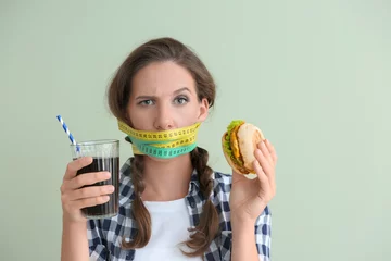 Poster Emotional woman with measuring tapes around her mouth and unhealthy food on color background. Diet concept © Pixel-Shot