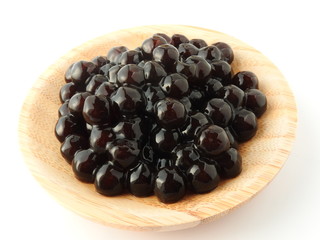 High angle view of tapioca ball (also known as boba in bubble tea) on wooden plate isolated on white background. Ingredients for making pearl milk tea and shaved ice at dessert shop. Food concept.
