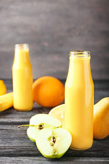 Bottle of tasty yellow smoothie and fruits on wooden table