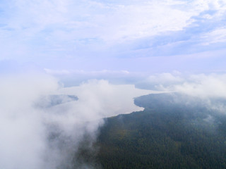 Aerial Drone view clouds over the green forest and lake. Low lying cloud. Aerial view of over tropical rainforest. Above the clouds in the sky. Big clouds. Atmosphere. Top view from drone