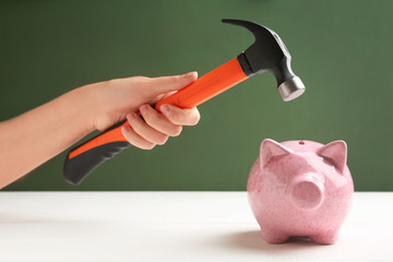 Woman holding hammer over piggy bank on color background