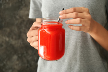 Woman holding mason jar of tasty red smoothie on grey background