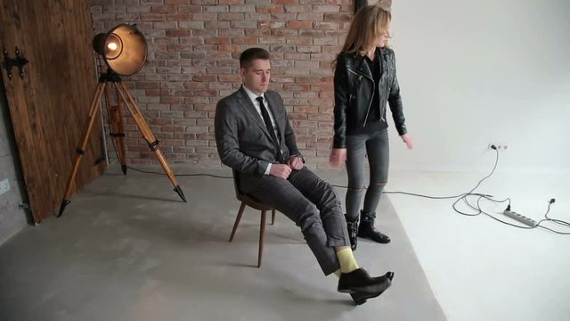 Fashionable couple in modern clothes posing in a photo Studio against a brick wall. A man in a suit, a girl in ripped jeans and a leather jacket.