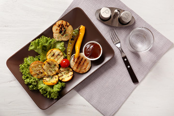 Plate with tasty grilled vegetables and sauce on light table