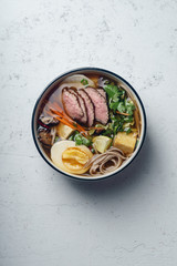 Miso ramen with roasted beef, shiitake mushrooms, fried tofu, leek and eggs on concrete background. Top view. Lunch in asian style