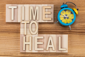 time to heal-  text in vintage letters on wooden blocks with alarm clock. Medicine concept