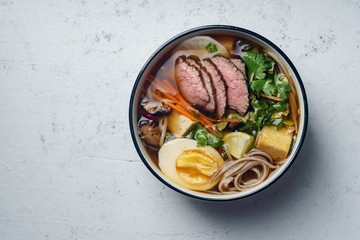 Miso ramen with roasted beef, shiitake mushrooms, fried tofu, leek and eggs on concrete background. Top view. Lunch in asian style