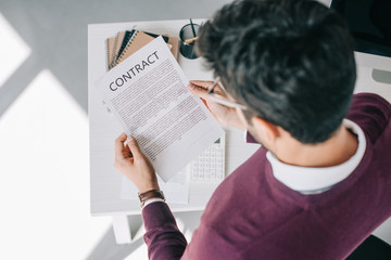 overhead view of designer in burgundy sweater reading contract in office