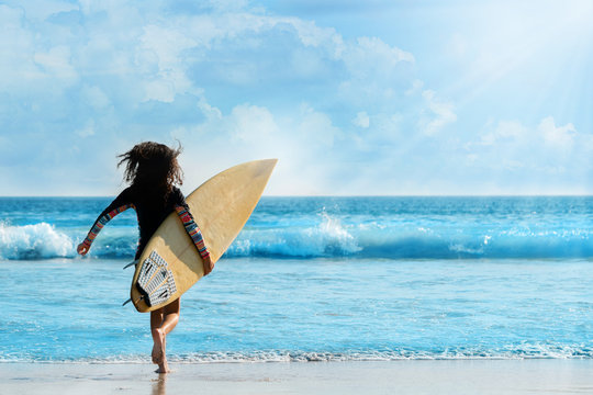 Girl holding surfboard running down to sea. Bright blue sea in the evening for surfing. During long weekend of summer Feel refreshed and relaxed. sunscreen help protect the skin against sun exposure.