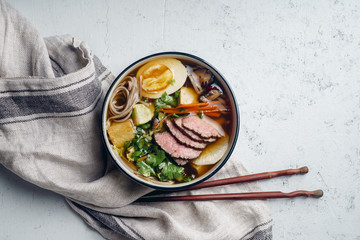 Miso ramen with roasted beef, shiitake mushrooms, fried tofu, leek and eggs on concrete background. Top view. Lunch in asian style
