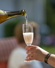 Glass of champagne. Pouring from the bottle outdoors. Glass half full