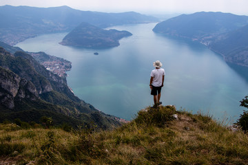 A Man on a Cliff in Mountains next to Italian Alpine Lake Iseo and the near Mountains, the lake Shore and island of Monte Isola whre you can hike