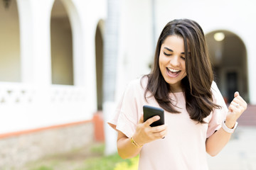 Woman Receiving Good News On Smartphone Outdoors