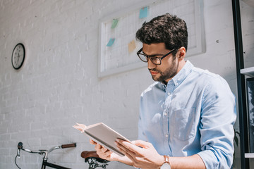 handsome architect in glasses reading book in office