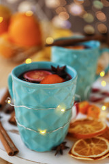 Cup of delicious mulled wine with Christmas garland on table