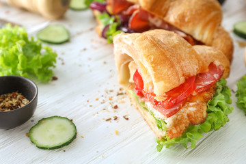 Tasty croissant sandwich with meat and fried egg on white wooden table