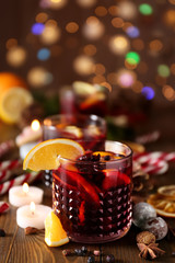 Glass of delicious mulled wine on wooden table against blurred lights